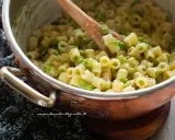 Un primo piatto invitante: pasta e piselli cremosa, mescolata con un cucchiaio di legno in una pentola di rame.