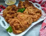 Goldbraun paniertes Schnitzel, perfekt zubereitet, liegt auf einem weißen Teller, garniert mit Petersilie und Radieschen.