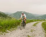 Kolarz na rowerze pokonuje krętą drogę z **gravel co to** w tle górskiego krajobrazu.