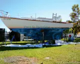 Un bateau est sur des chandelles, prêt pour une peinture. La ligne de flottaison est visible sur la coque bleue. Un homme travaille sur le bateau.