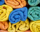 Rolled towels in vibrant colors: yellow, orange, blue, and green. These are made from biodegradable fabric, perfect for eco-conscious living.