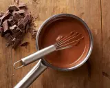 Chocolat fondu qui durcit dans une casserole, avec des morceaux de chocolat à côté sur une planche en bois.
