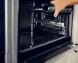 Wasser wird aus einer Flasche in einen modernen **Hydrolyse Backofen** gegossen, um die Reinigung zu erleichtern.