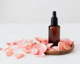 Flacon d'huile essentielle ambré entouré de pétales de rose. Un soin doux pour une femme enceinte.