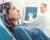 Kobieta w czepku EEG podczas badania VEP. Lekarz analizuje wyniki na ekranie.