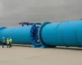 Große blaue Kabeltrommeln mit Arbeitern davor, Kräne im Hintergrund.