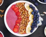En färgglad acai bowl med jordgubbar, banan, blåbär och granola. Serverad med mandlar och kokosflingor vid sidan.