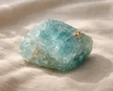 Una grezza acquamarina pietra, con sfumature azzurre e inclusioni dorate, riposa su un tessuto chiaro.