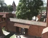Wielki zamek w Malborku, ceglane mury, dziedziniec z drzewami i ludźmi spacerującymi pośród zabytkowej architektury.