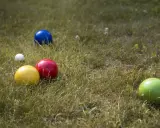 Boules colorées (jaune, rouge, bleu, vert) et une petite blanche sur l'herbe, prêtes pour un concours de pétanque.