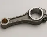 Una biela de motor de metal gris con un casquillo de bronce en un extremo y un perno en el otro.