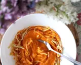 Pyszny przepis na sos do spaghetti, podany z makaronem w białej misce. W tle kwitnące kwiaty.