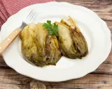 Deux endives caramélisées à la poêle, garnies de persil, sur une assiette blanche avec une serviette à carreaux rouges et une fourchette.