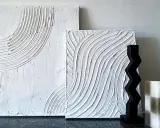 Två vita texturtavlor, en med bågformade linjer och en med vågformade, skapade med spackel. Bredvid står en svart zickzack-figur och en rutig ljus.