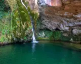 La cascada del río Carbo cae en una poza de agua verde esmeralda, rodeada de rocas cubiertas de musgo y vegetación exuberante.