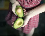 Hände halten eine aufgeschnittene Avocado, bereit für eine pflegende Avocado-Maske für die Haare.