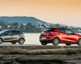 Dos Mazda, uno gris y otro rojo, junto al mar. La fiabilidad Mazda se refleja en su diseño y presencia.