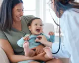 Glad mamma ser sitt barn få ett års vaccin. Läkaren lyssnar på barnets hjärta med stetoskop.
