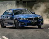Niebieskie BMW 320i w zakręcie, unosząc tumany kurzu. Dynamiczna jazda na torze.