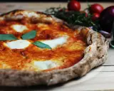 En perfekt pizza på grillen, med smält mozzarella och färsk basilika. Tomater och vitlök i bakgrunden.