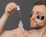Homme appliquant un sérum, se demandant acide glycolique combien de fois par semaine. Patchs noirs sous les yeux pour un soin ciblé.