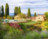 Vacanze in Toscana dove andare? Un casale in pietra con piscina, circondato da cipressi e un giardino fiorito.
