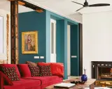 Sofá rojo vibrante con cojines estampados, pared azul petróleo y detalles rústicos. ¡Los mejores colores para pintar una casa!