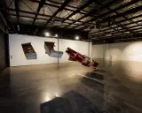 Suspended sculptures of weathered wood and metal hang in the spacious praxis gallery, casting long shadows on the concrete floor.