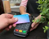 Pago sin contacto con una tarjeta prepago. Una mano acerca una tarjeta de colores a un terminal de pago.