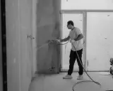 Man sprutar färg på en vägg inomhus, en del av arbetet med fasad hus.