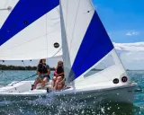 Deux jeunes femmes naviguent sur un voilier RS Venture par une journée ensoleillée. L'eau scintille sous le ciel bleu.