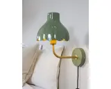 A green scalloped lampshade with a yellow interior, mounted on a gold arm attached to a green wall plate.