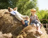 Dzieci odpoczywają na sianie podczas pobytu na agroturystyce ze zwierzętami. Chłopiec leży z rękami za głową, a dziewczynka siedzi w słomkowym kapeluszu.