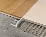 Un battiscopa metallico crea abbinamenti quando mancano le piastrelle del pavimento, unendo legno e ceramica su un sottofondo grezzo.