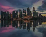 Wieżowce w Singapurze odbijają się w wodzie o zachodzie słońca. To miasto-państwo, gdzie leży Singapur, zachwyca nowoczesną architekturą.
