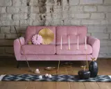 En dyr soffa i sammet, rosa, med dekorativa föremål som en golfklubba, bollar, ljusstakar och ananasskulpturer.