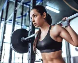 Eine athletische Frau, die als Bodybuilderin trainiert, hebt eine Langhantel im Fitnessstudio.