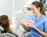 Uśmiechnięta higienistka stomatologiczna pokazuje pacjentce, jak prawidłowo szczotkować zęby na modelu szczęki.