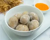 Un tazón blanco lleno de papas arrugadas, cubiertas de sal, junto a un pequeño cuenco con mojo rojo.