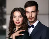 Elegancka para, niczym koziorożec i baran, pozuje do zdjęcia. Ona w ciemnej sukni, on w granatowym garniturze.