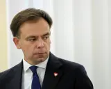 Minister finansów w granatowym garniturze i niebieskim krawacie, z przypinką w kształcie serca na klapie marynarki.