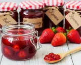 Bocaux de confiture de fraise faits maison, avec des fraises fraîches et une cuillère remplie de confiture.