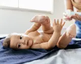 Uroczy noworodek leży na granatowym kocyku, podnosząc nóżki. Mama przygotowuje się do masażu brzuszka, by ulżyć mu w **gazach u noworodka**.