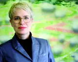 Frauke Burgdorff, eine Frau mit kurzen blonden Haaren und Brille, blickt lächelnd in die Kamera. Sie trägt einen grauen Blazer.