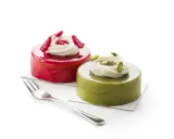 Deux petits gâteaux brillants, l'un rouge vif, l'autre vert avec un glaçage pistache, ornés de crème et de fruits.