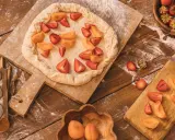 Préparation d'un crumble abricot et fraises sur une planche en bois, avec des œufs et des fruits frais à proximité.