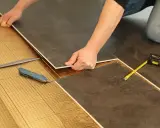 Pose de dalles de sol sur une sous-couche isolante. Un cutter et un mètre sont à portée de main pour comment isoler un sol efficacement.