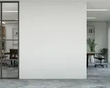 Un moderno tabique de cristal separa una sala de reuniones con estanterías de madera de una oficina con vistas a un jardín frondoso.