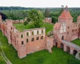 Ruiny ceglanego zamku w Szembarku otoczone zielenią. Widać most nad fosą, wieże i fragmenty murów obronnych.