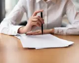 Dłoń z długopisem nad stosem papierów, gotowa do spisania, jak złożyć skargę na kuriera InPost.